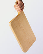 Hand holding a wooden cutting board against a light background