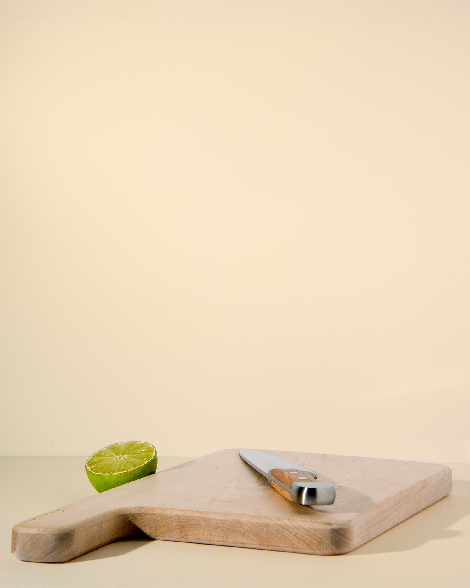 Wooden cutting board with a knife and half a lime on a beige background